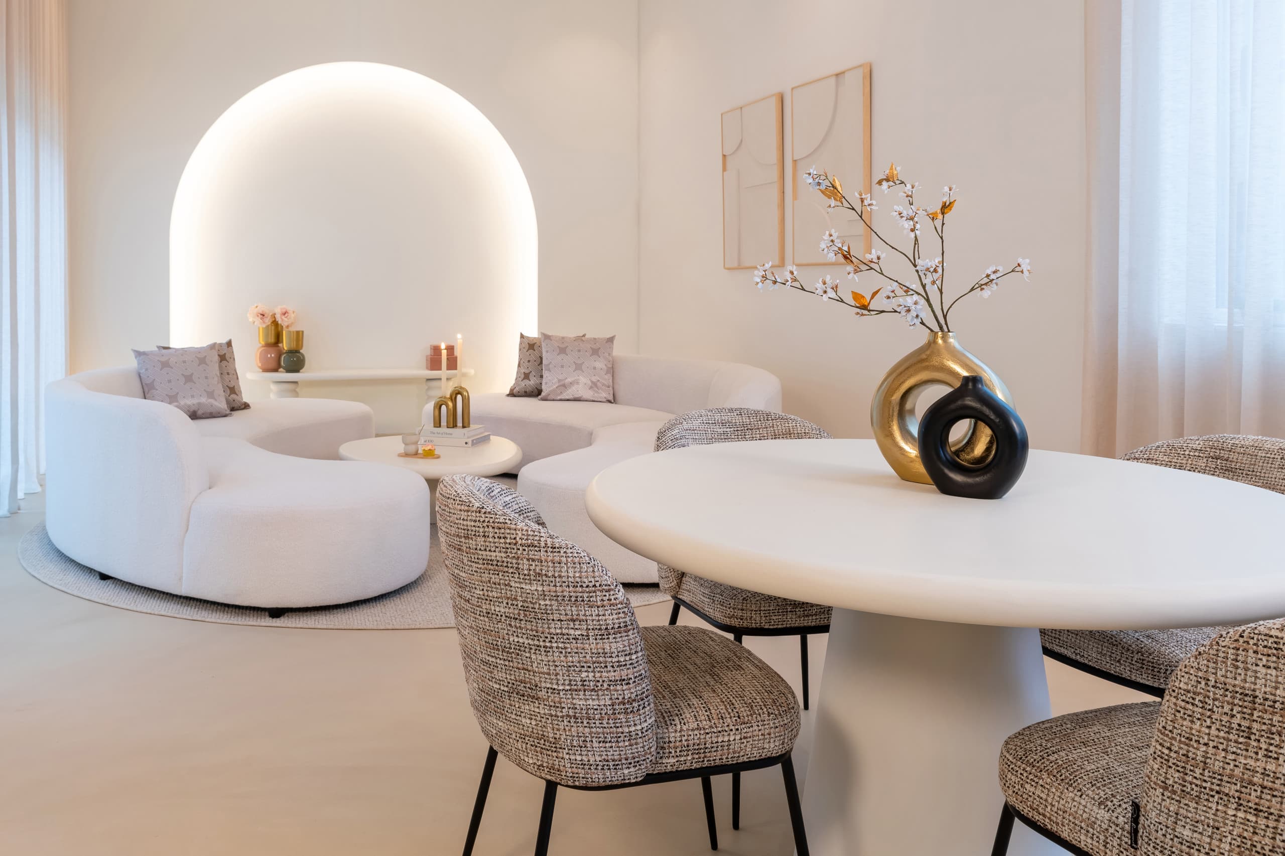 Eetkamerstoelen met gemêleerde structuurstof rond een ronde witte eettafel, met een gouden en een zwarte vaas op het blad
